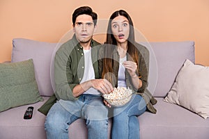 Photo of stupor guy lady fellows sit couch watch horror series eat pop corn isolated over beige color background