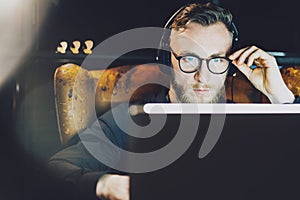 Photo stylish bearded man wearing glasses working modern loft office. Young banker sitting vintage chair,listening music