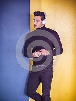 Photo of a stylish man enjoying music while leaning against a wall