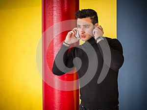 Photo of a stylish man enjoying music while leaning against a wall