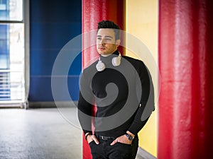 Photo of a stylish man enjoying music while leaning against a wall
