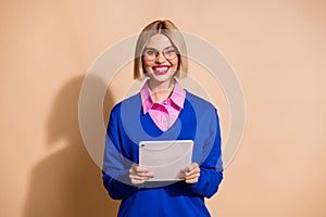 Photo of successful cheerful girl toothy smile hold use tablet coworking isolated on beige color background
