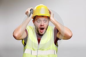 Photo of surprised builder in yellow helmet with walkie talkie on empty gray background.