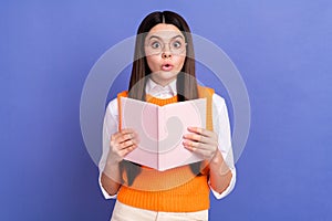 Photo of surprised girl encyclopedia shocked amazed reading book pouted lips unexpected information isolated on purple