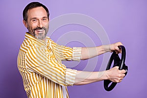 Photo of sweet attractive mature man dressed striped shirt driving car holding steering wheel smiling isolated violet