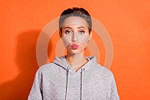 Photo of sweet charming young woman dressed grey hoodie sending you kiss isolated orange color background