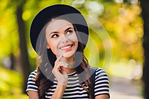 Photo of sweet dreamy young woman dressed striped outfit cap backpack walking finger chin thinking smiling outside