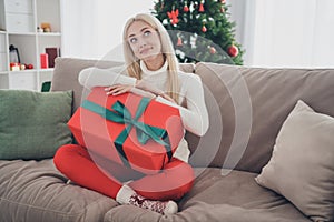 Photo of sweet dreamy young woman dressed white sweater holding gift box smiling indoors room home house