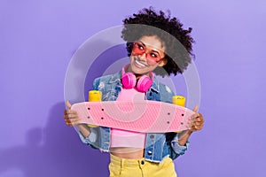 Photo of sweet dreamy young woman wear jeans jacket headphones long board empty space isolated violet color background