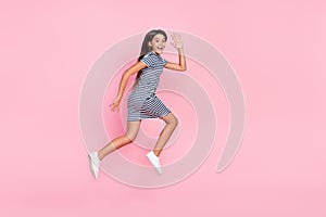 Photo of sweet friendly girl wear striped dress jumping high running waving arm isolated pink color background