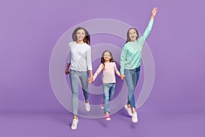 Photo of sweet funny daughters mom dressed casual sweaters holding hands jumping high isolated purple color background