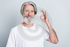 Photo of sweet positive retired man wear white t-shirt smiling showing okey sign isolated grey color background
