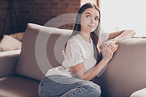 Photo of sweet thoughtful young lady wear white t-shirt sitting sofa smiling having rest indoors house room