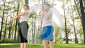 Photo of teenage boy doing yoga with his mother on grass park. Family doing fitness and stretching exercises together at