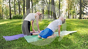 Photo of teenage boy doing yoga with his mother on grass park. Family doing fitness and stretching exercises together at