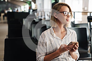 Photo of thinking blonde woman typing on smartphone while sitting