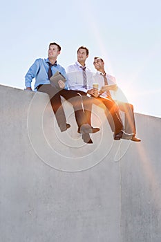 Photo of thoughtful businessmen sitting while using digital tablet in office rooftop