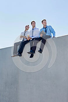Photo of thoughtful businessmen sitting while using digital tablet in office rooftop