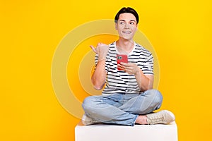 Photo of thoughtful dreamy man wear striped t-shirt writing sms modern gadget thumb empty space isolated yellow color