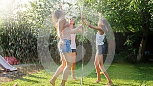 Photo of three cheerful teenage girls dancing in the backyard garden udner garden water hose