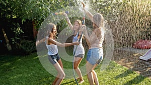 Photo of three cheerful teenage girls dancing in the backyard garden udner garden water hose