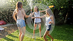 Photo of three cheerful teenage girls dancing in the backyard garden udner garden water hose