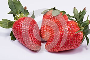 Photo of three fresh red strawberries with strawberry leaf isolated on white background