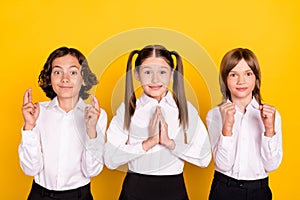 Photo of three hopeful schoolchildren crossed fingers plead wear white shirt isolated yellow color background