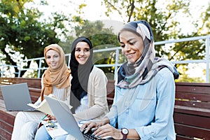 Photo of three islamic girls wearing headscarfs resting in green park