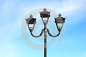 photo of three modern metal LED lamps in vintage style on a single post against a blue sky