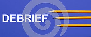 Photo of three orange pencils on a blue background with the text DEBRIEF