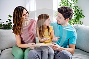 Photo of three people sit couch little kid read book story tell her parents mommy daddy in house indoors