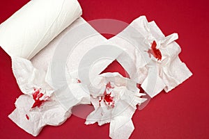 A photo of three used bloody toilet paper and toilet paper roll on the red background. Menstrual, hemorrhoids bleeding. Bloo