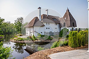 Photo of a three-story house with a reed roof, chimneys and dormers on the banks of the river bed. Blue sky. Horizontal