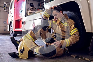 Photo of tired fireman sitting on floor near fire truck