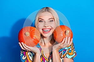 Photo of toothy beaming cute girl with bob hairdo dressed print shirt hold two squash on cheekbones isolated on blue