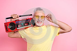 Photo of toothy beaming man with beard dressed yellow t-shirt holding boombox on shoulder touch sunglass isolated on