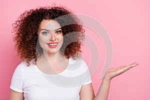 Photo of toothy beaming woman with perming coiffure dressed white t-shirt palm show object empty space isolated on pink