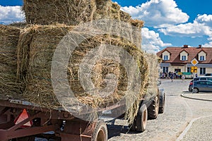 Photo of a tractor hauling hay for animal feed through the cobbled streets of a small town with houses with tiled roofs against a