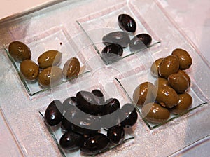 Photo transparent glass dish with four sections, which laid out green and black olives.