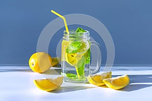 Photo of a transparent glass mug filled with water, sliced â€‹â€‹lemon and mint leaves with a yellow straw