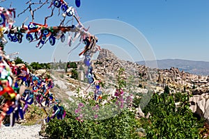 In the photo, a tree hung with amulets in the form of an eye against the background of an ancient cave settlement called