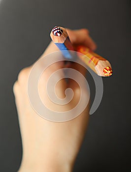 Photo of two colored pencils in a person& x27;s hand. Black background. The hand is blurred. View from above.