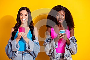 Photo of two excited young girl happy positive smile amazed surprised use smartphone isolated over yellow color