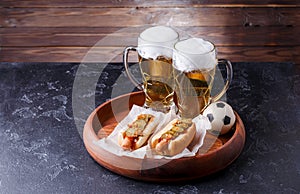 Photo of two glasses of beer and hot dogs on wooden tray with football