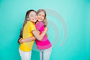 Photo of two hugging girls creating copyspace loving each other as best friends while isolated with teal background