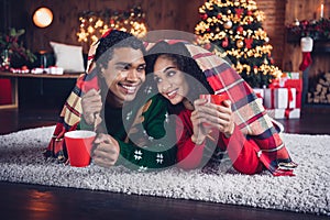 Photo of two idyllic partners laying carpet floor under warm blanket drink hot chocolate cozy festive christmas
