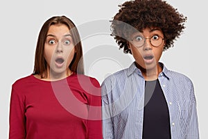 Photo of two impressed women recieve shocking news, keep jaw dropped from emotions, stare impressed at camera, open