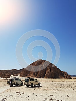 Photo of two jeeps on background of mountain, sand blue sky