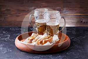 Photo of two mugs of beer and hot dogs on wooden tray